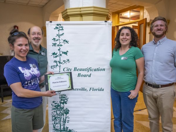 People standing in front of a sign that says "City Beautification Award" while one person holds a plaque.